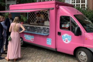 Gruppe von Menschen, die um einen pinken Foodtruck stehen, der Eisrollen und Hamburger serviert